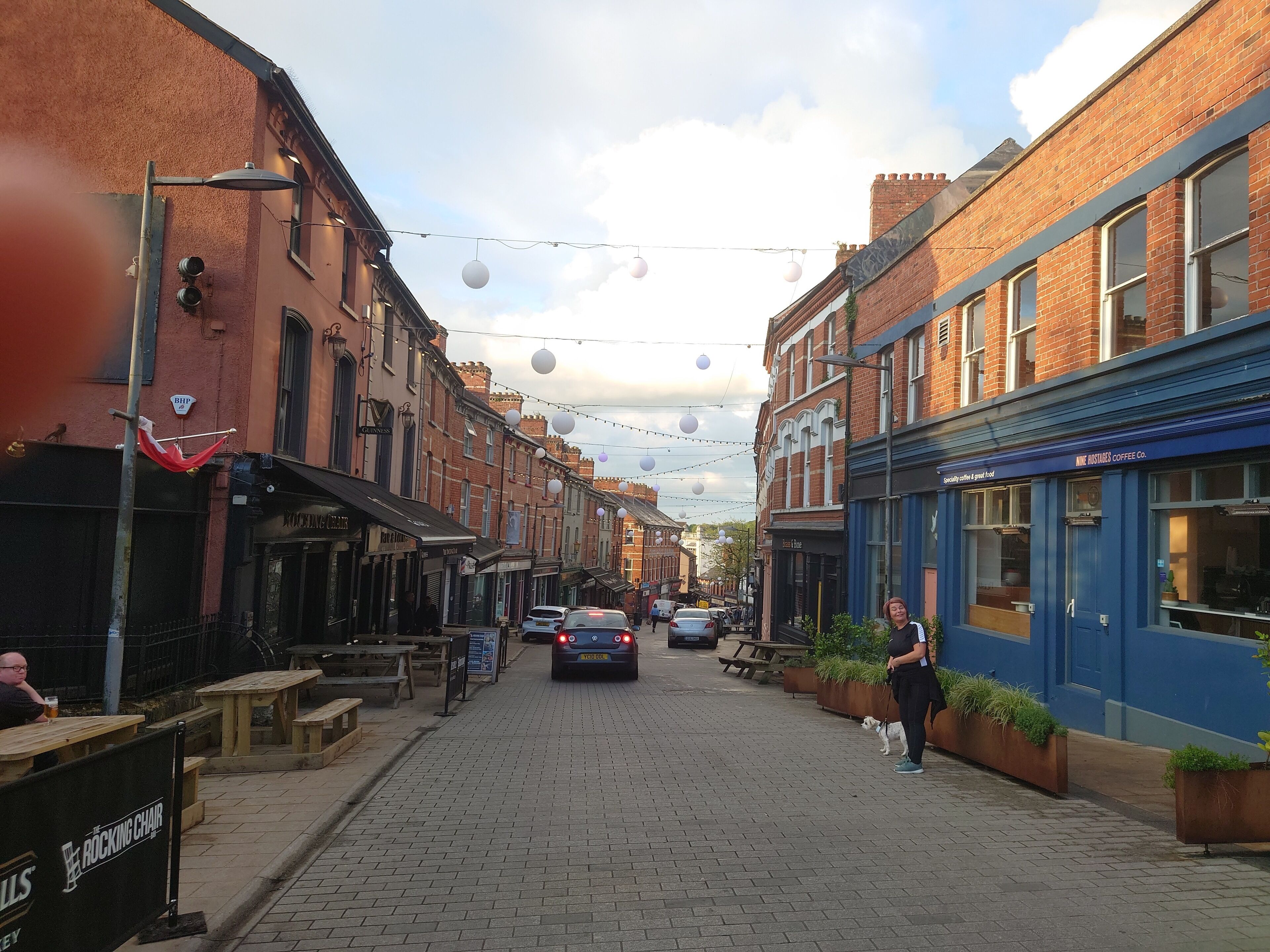A narrow street lined with brick buildings, outdoor seating, and string lights.
