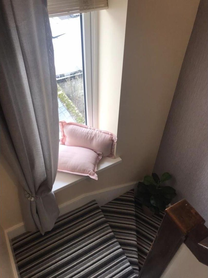 A stairway with striped carpeting leading to a window sill with two pink pillows.