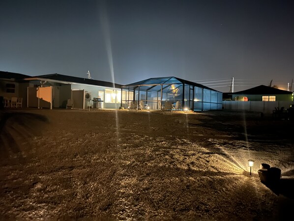 A greenhouse structure with a glass roof, surrounded by a gravel driveway and adjacent buildings.