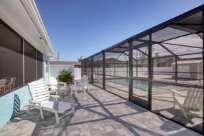 Ein überdachter Außenbereich mit Pool, weißen Stühlen und einem kleinen Tisch.