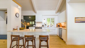 Une cuisine moderne dotée d’un îlot central, de tabourets de bar en bois et offrant une vue sur l’extérieur.