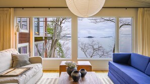 Un salon moderne doté d’une grande fenêtre donnant sur un lac et une île au loin.