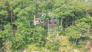 Une maison à deux étages entourée d’une forêt dense.