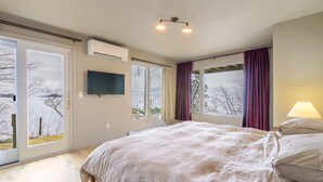 Une chambre à coucher avec un lit, une télévision, un climatiseur et de grandes fenêtres avec des rideaux.