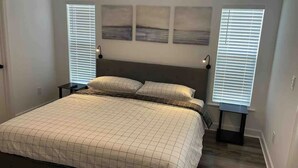 Ein Schlafzimmer mit einem Bett, zwei Nachttischen, einem Kopfteil und drei an der Wand befestigten Bildern.