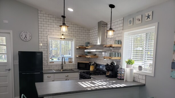Una cocina moderna con una isla central, taburetes de bar, un refrigerador negro e iluminación colgante.