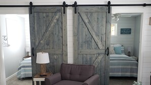 Una habitación con una gran puerta corrediza tipo granero, un sofá, una lámpara, una mesita con una planta y una cama con edredón a rayas.