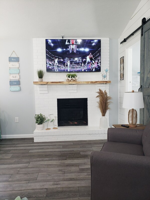 Ein Wohnzimmer mit Kamin aus weißen Ziegeln, einem flachbildfernseher darüber und einem Wandregal mit Dekorationselementen.