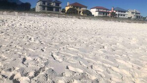 A sandy beach with footprints leading to a row of houses.