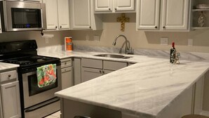 A kitchen with white cabinets, a stainless steel microwave, a stove, a sink, and a trash can.