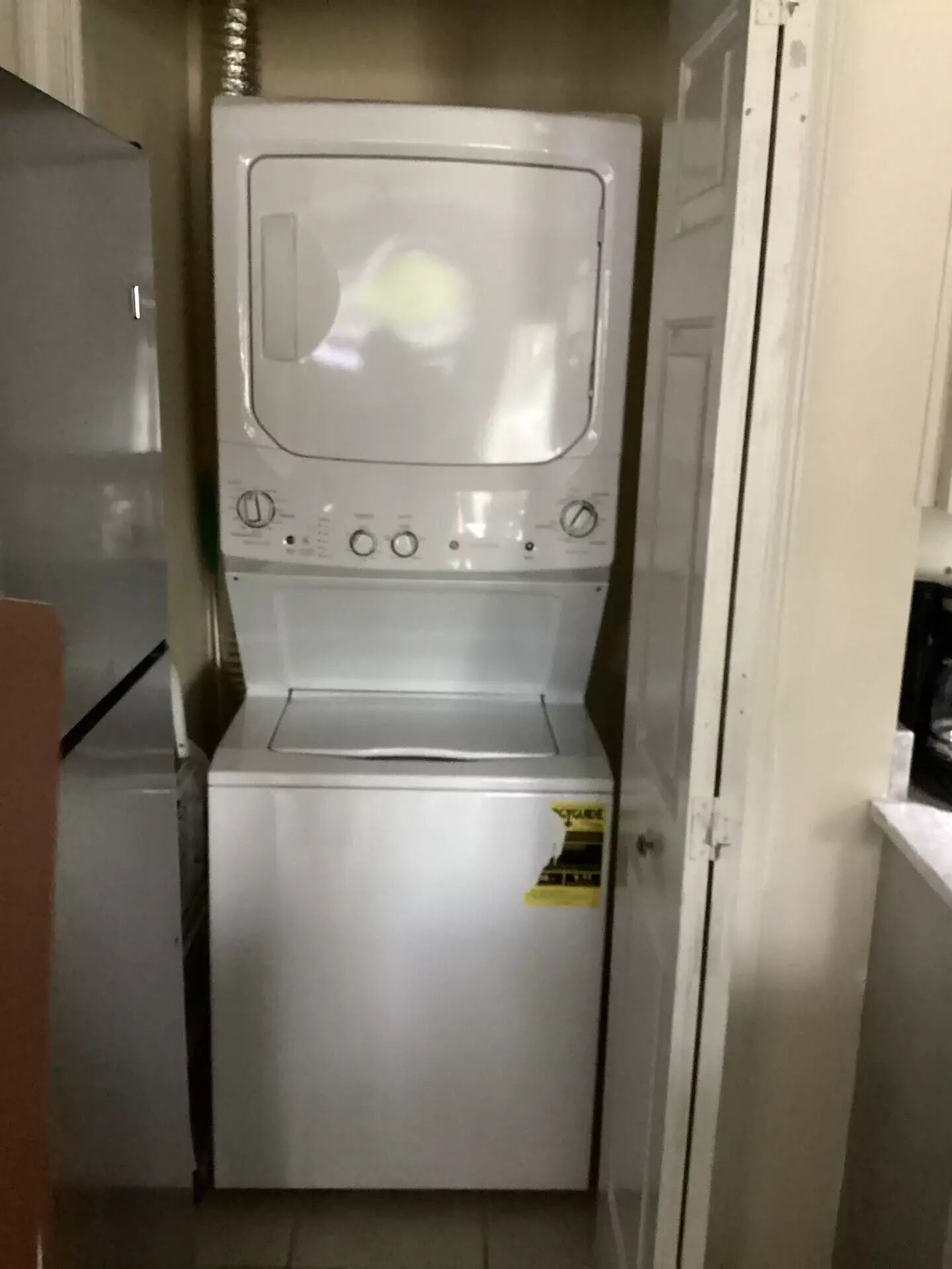 A compact laundry room with a washing machine and dryer, a small refrigerator, and a door leading to another room.