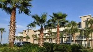 A multi-story hotel with palm trees and a parking area.