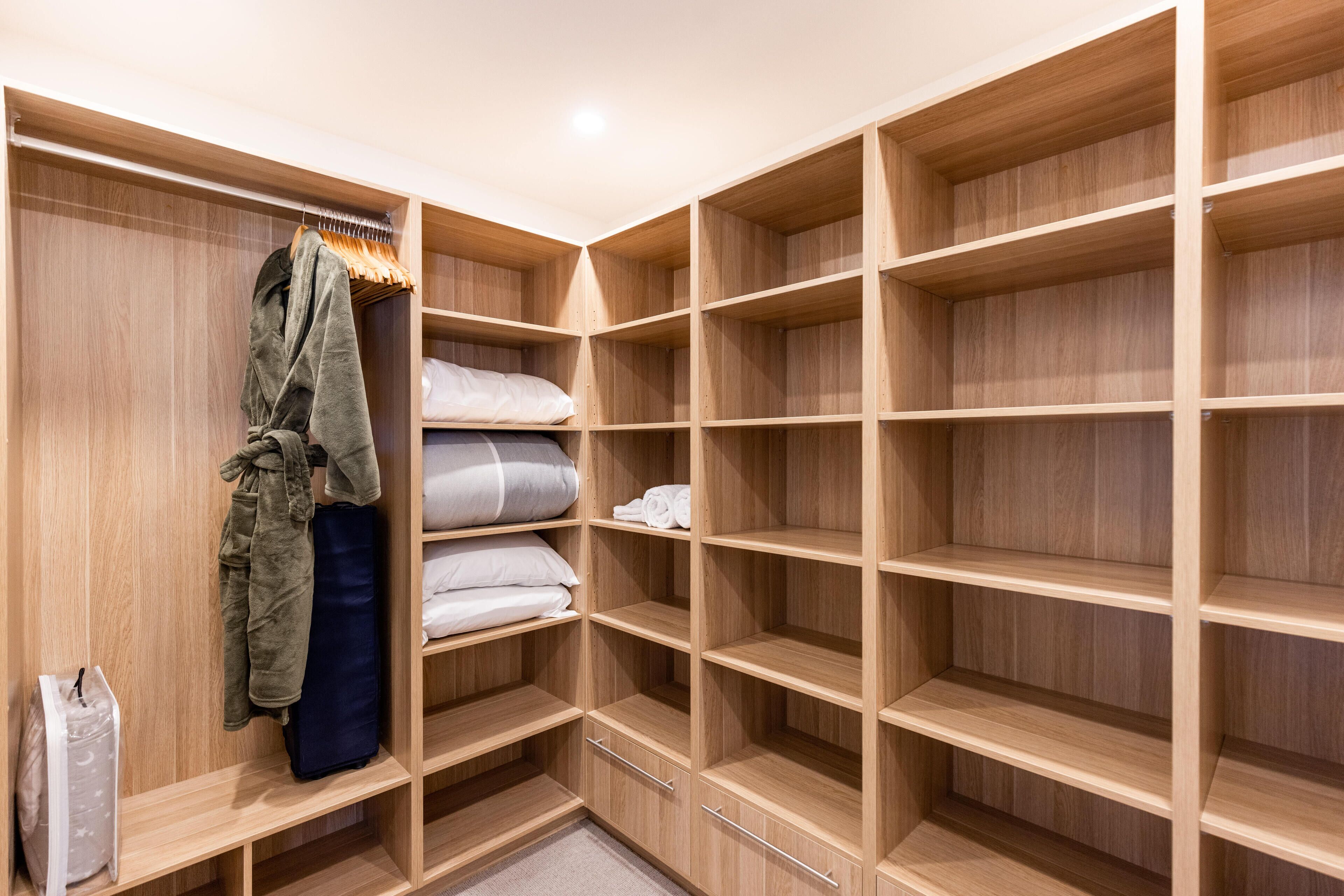 A walk-in closet with multiple wooden shelves and drawers, a hanging rack, and a suitcase.