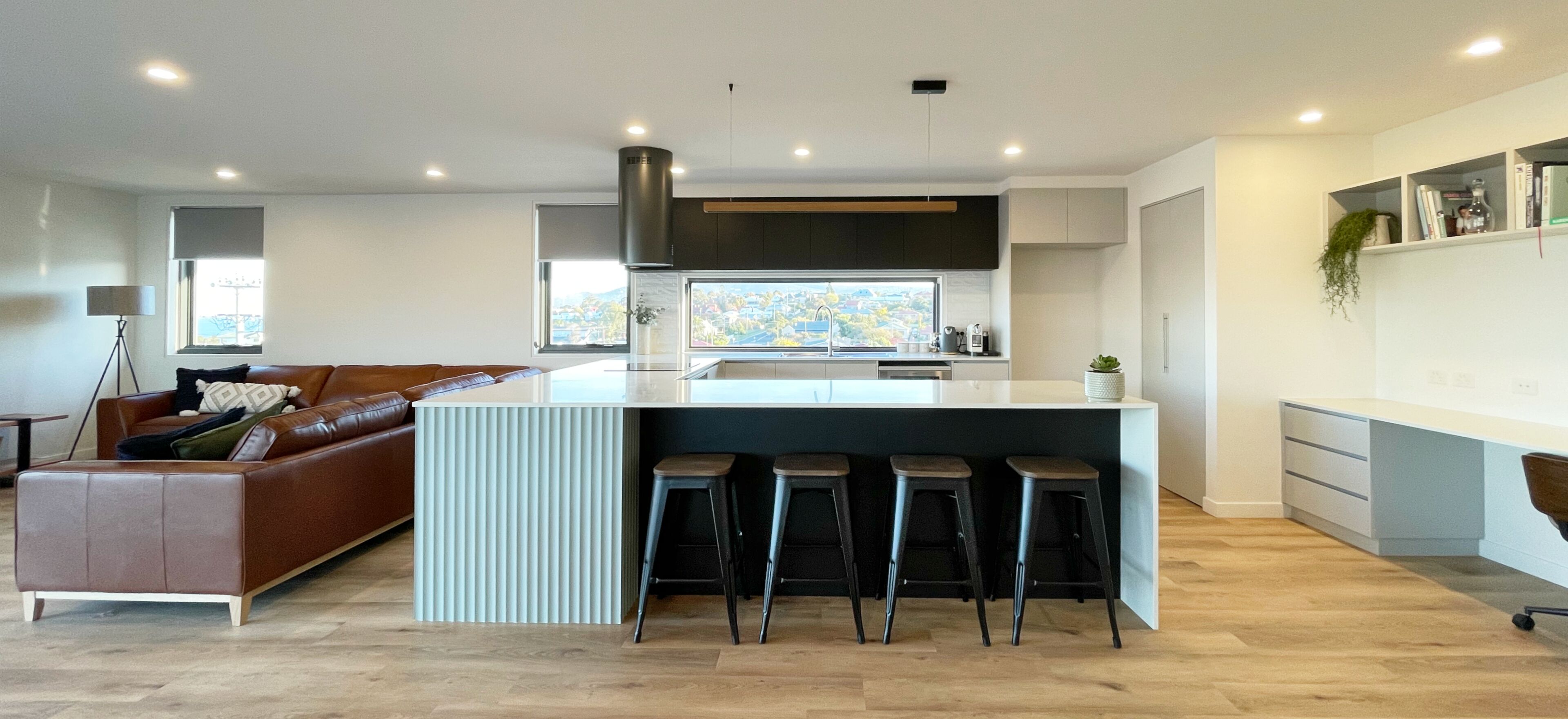 A modern kitchen with a central island, bar stools, and a view of a cityscape through large windows.