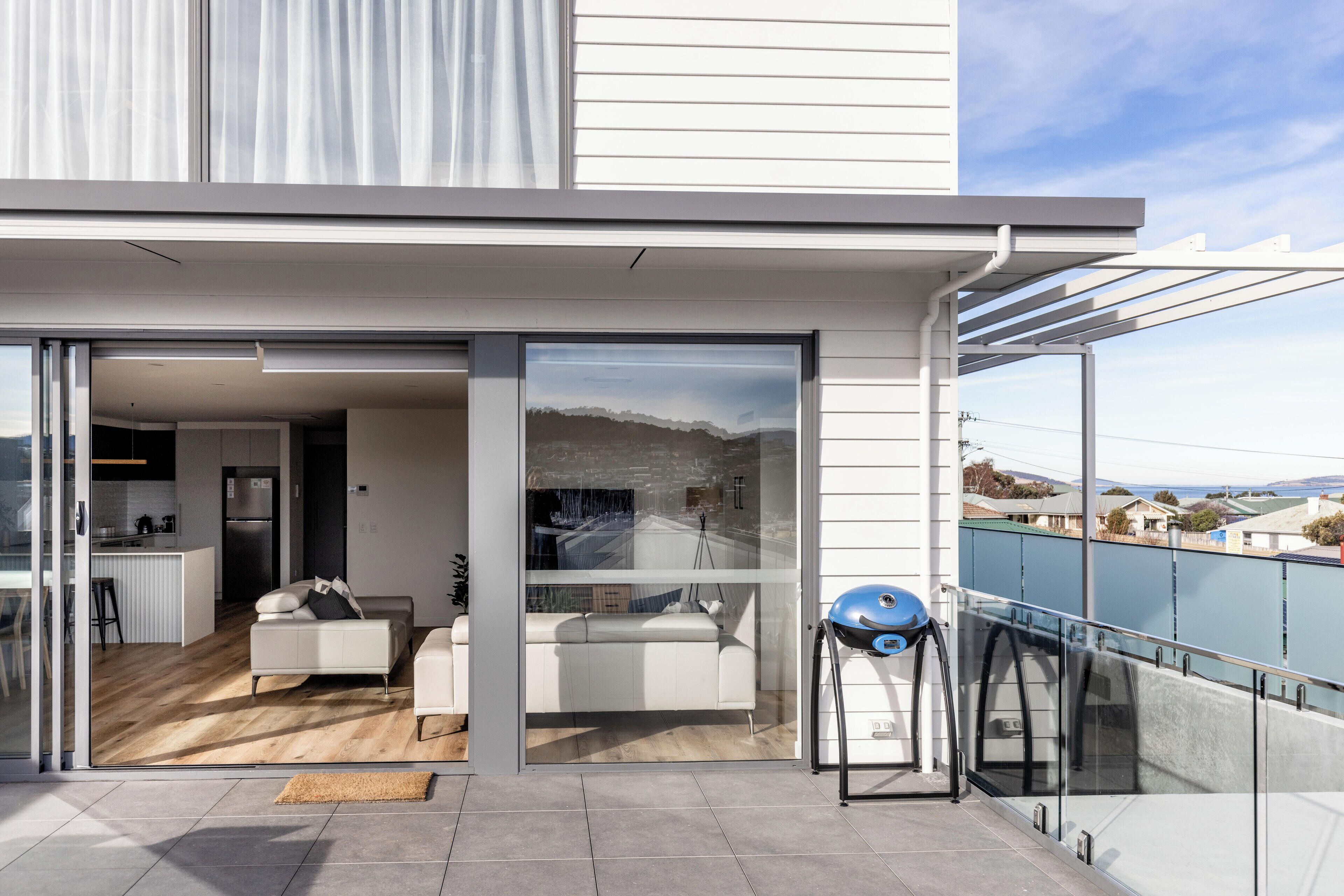Un apartamento moderno con una puerta de cristal que da a una sala de estar, un balcón con una silla azul y vistas a la ciudad.