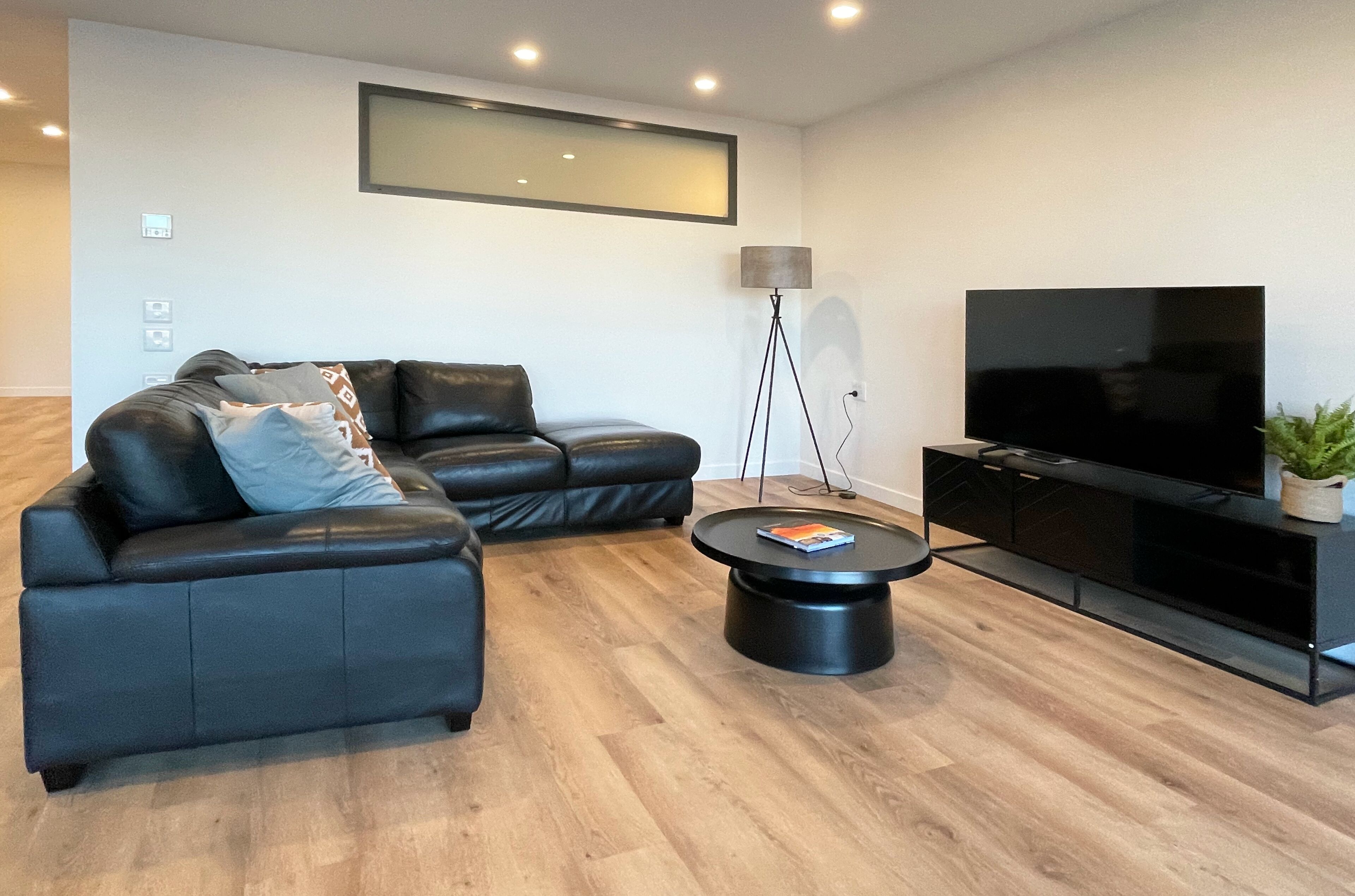 Una sala de estar moderna con un sofá de cuero negro, una mesa redonda de centro, un televisor de pantalla plana y una lámpara de pie.