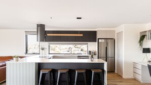 A modern kitchen with a central island, bar stools, a stainless steel refrigerator, and a large window offering a view. - Little Island Apartments (Bellerive)