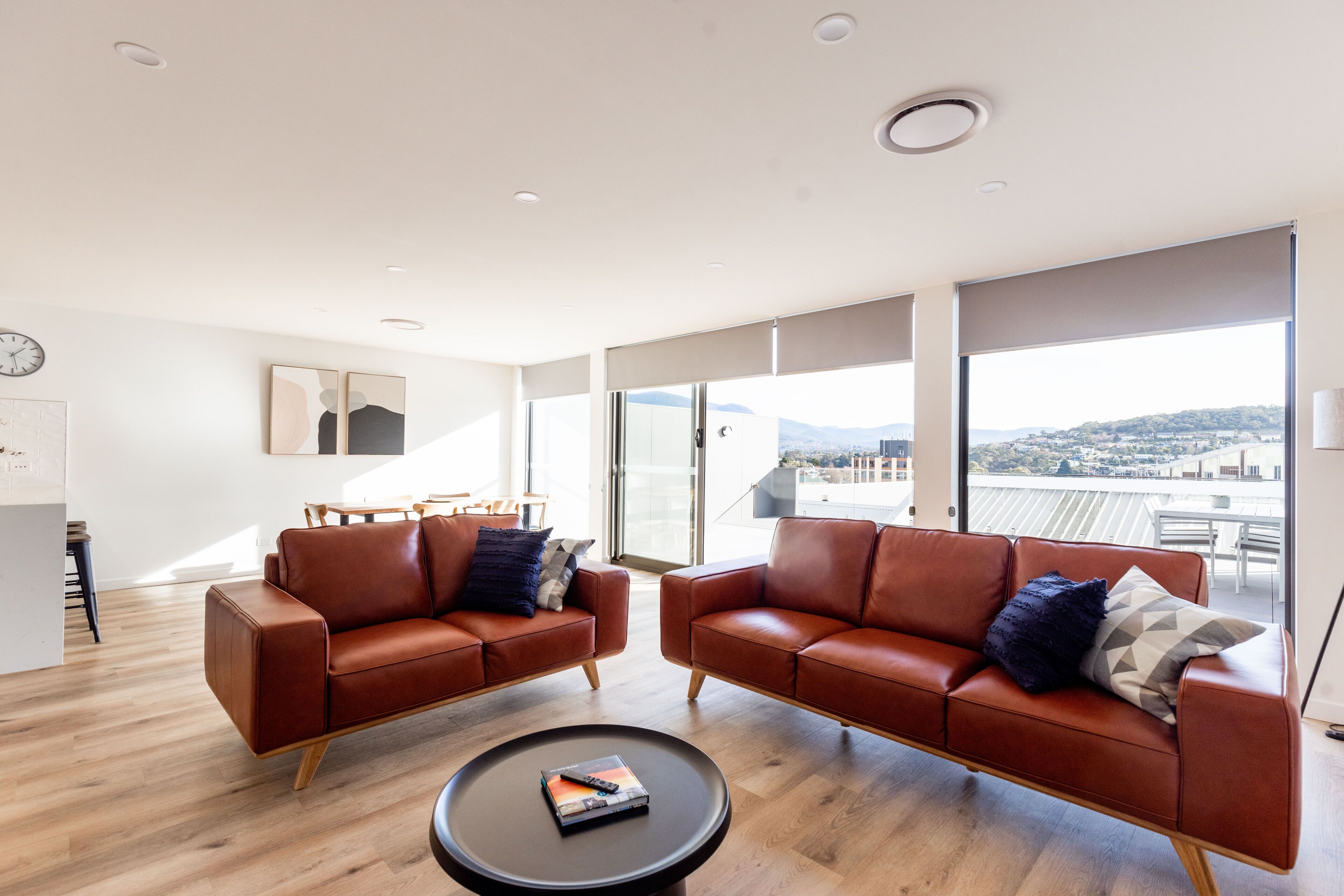 A modern living room with two leather sofas, a round coffee table, and large windows offering a city view.