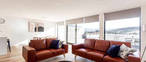 A modern living room with two leather sofas, a round coffee table, and large windows offering a city view.