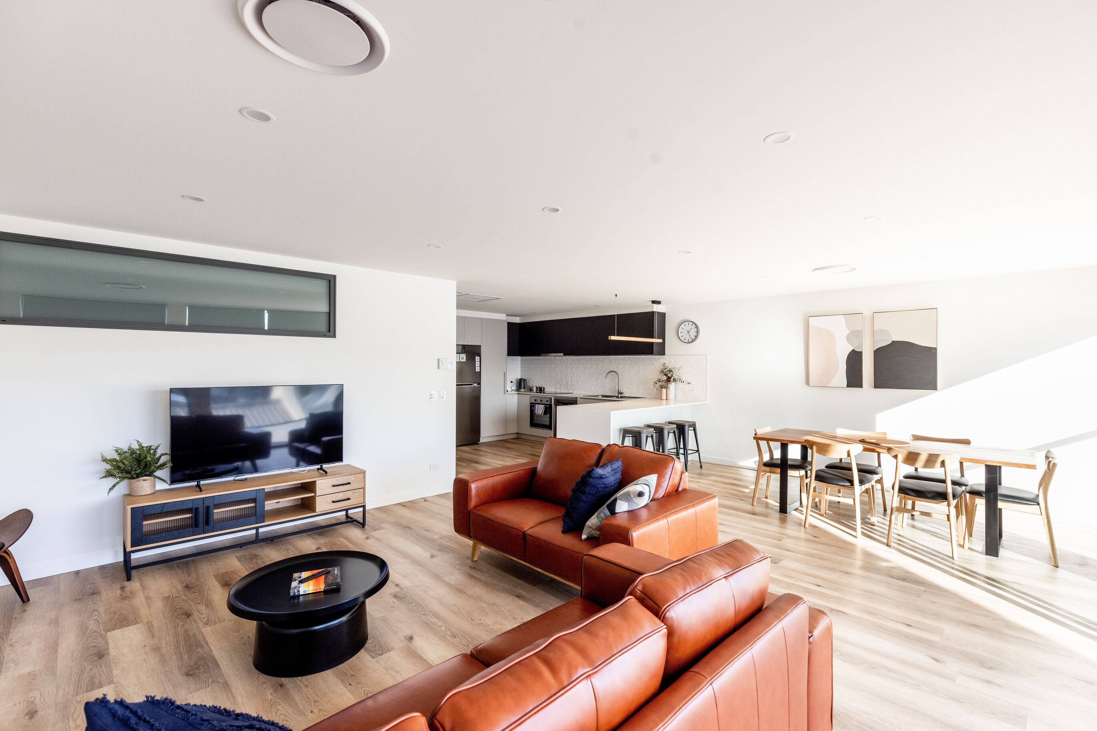 A modern living room with a sofa, coffee table, and TV. A kitchen is visible in the background.