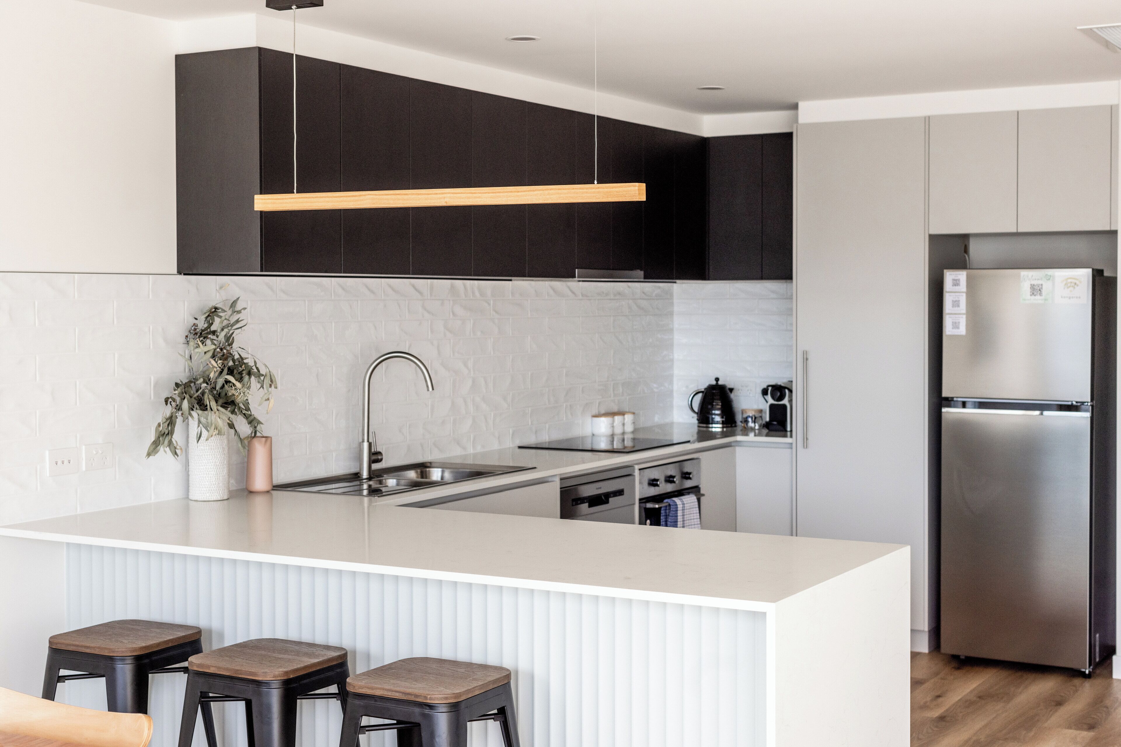 Une cuisine moderne dotée d’un grand îlot central, de meubles de rangement aux couleurs sombres, d’appareils électroménagers en acier inoxydable et d’un design minimaliste.