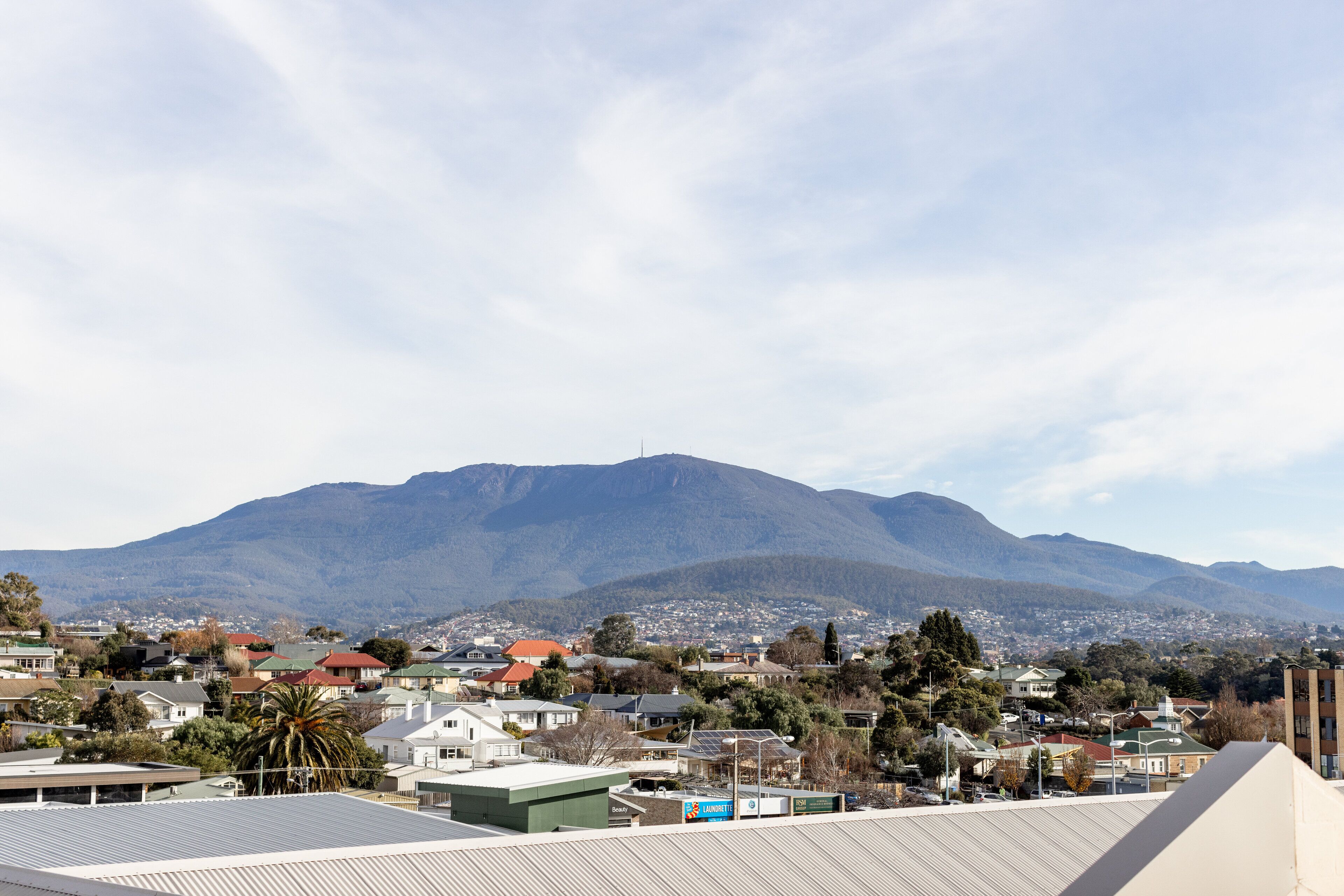 A residential area with houses, a prominent mountain in the background, and a clear sky.