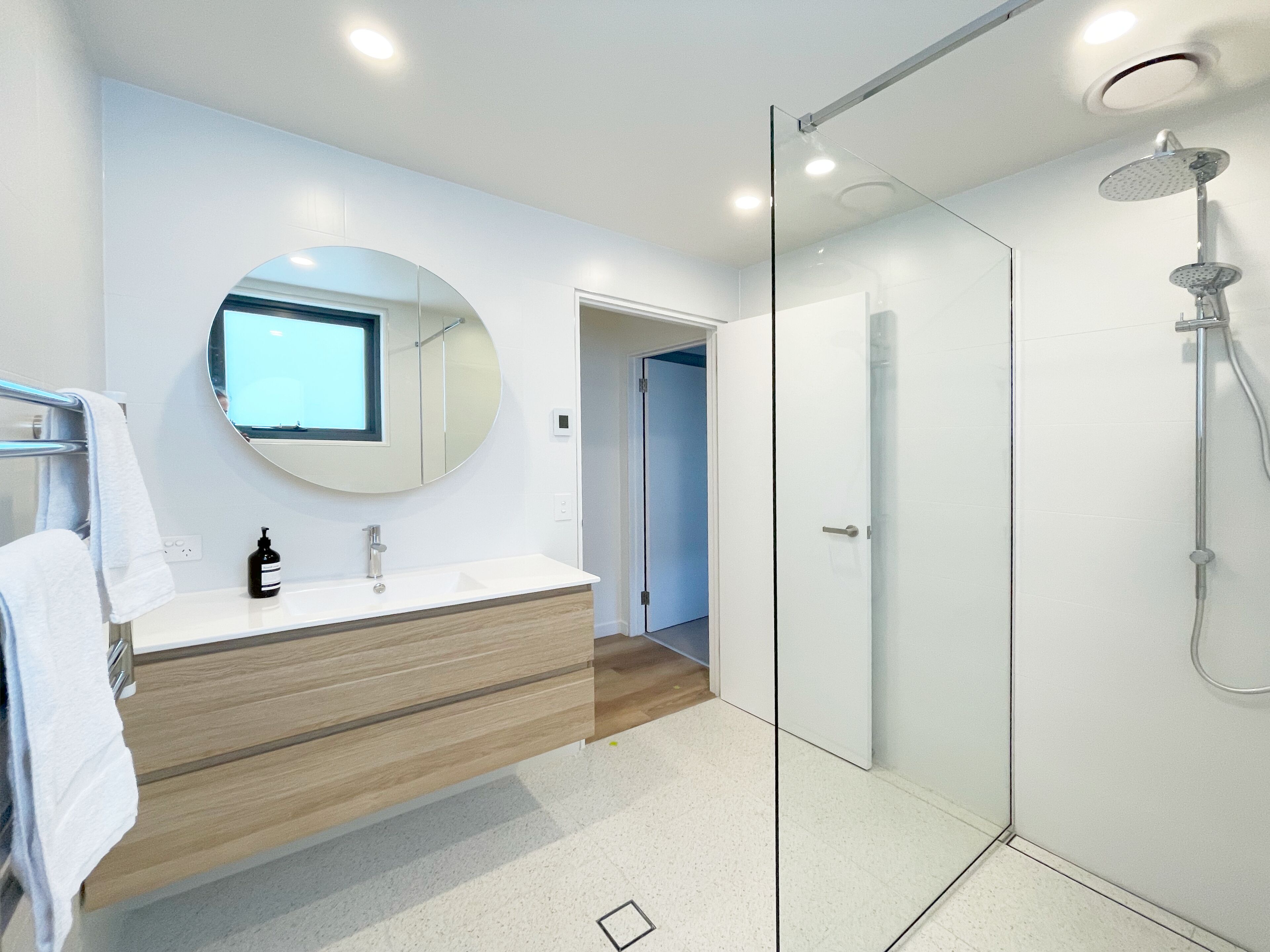 A modern bathroom with a glass-enclosed shower, a round mirror, and a wooden vanity.