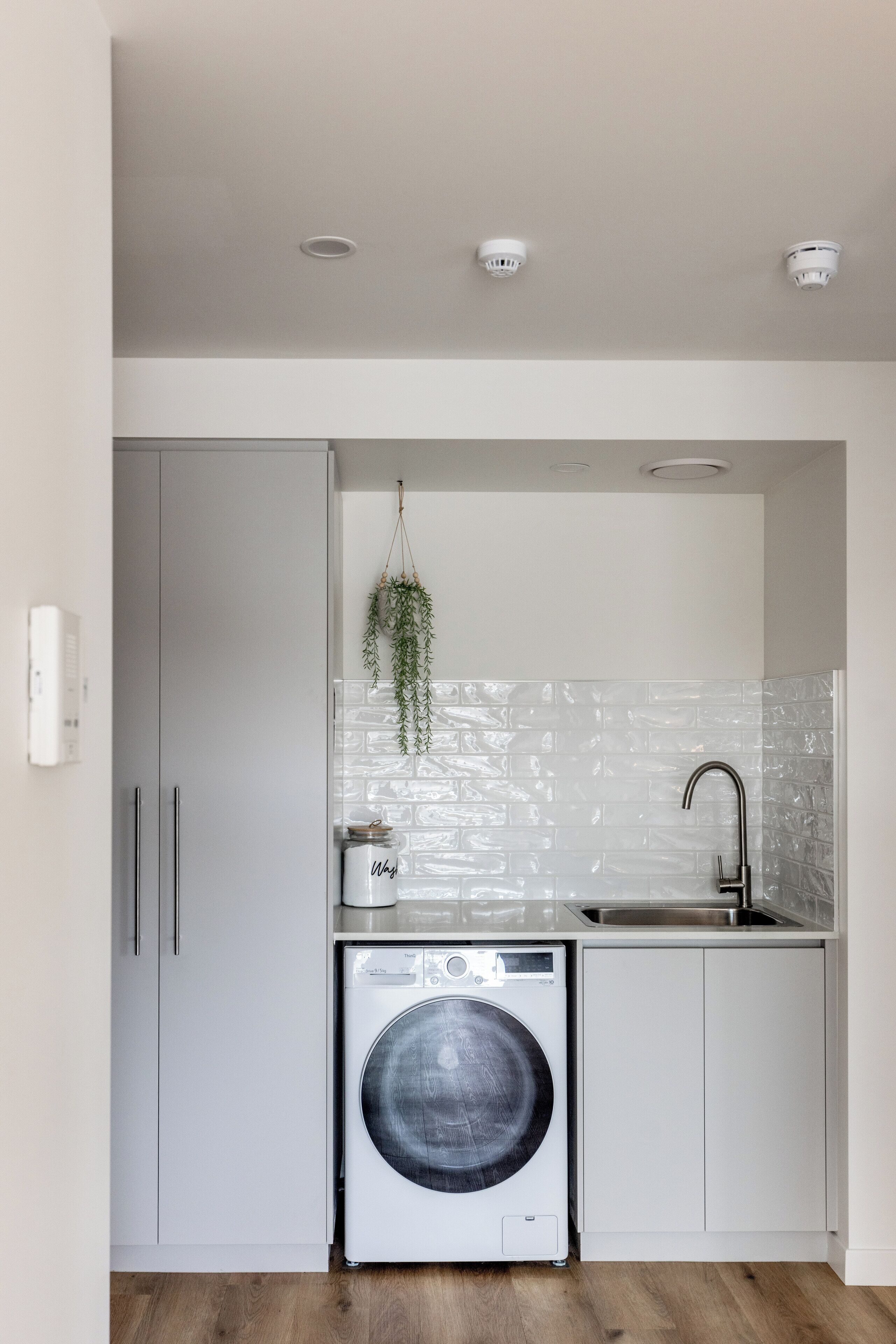 A compact kitchen with a washing machine, a hanging plant, and a tiled backsplash.