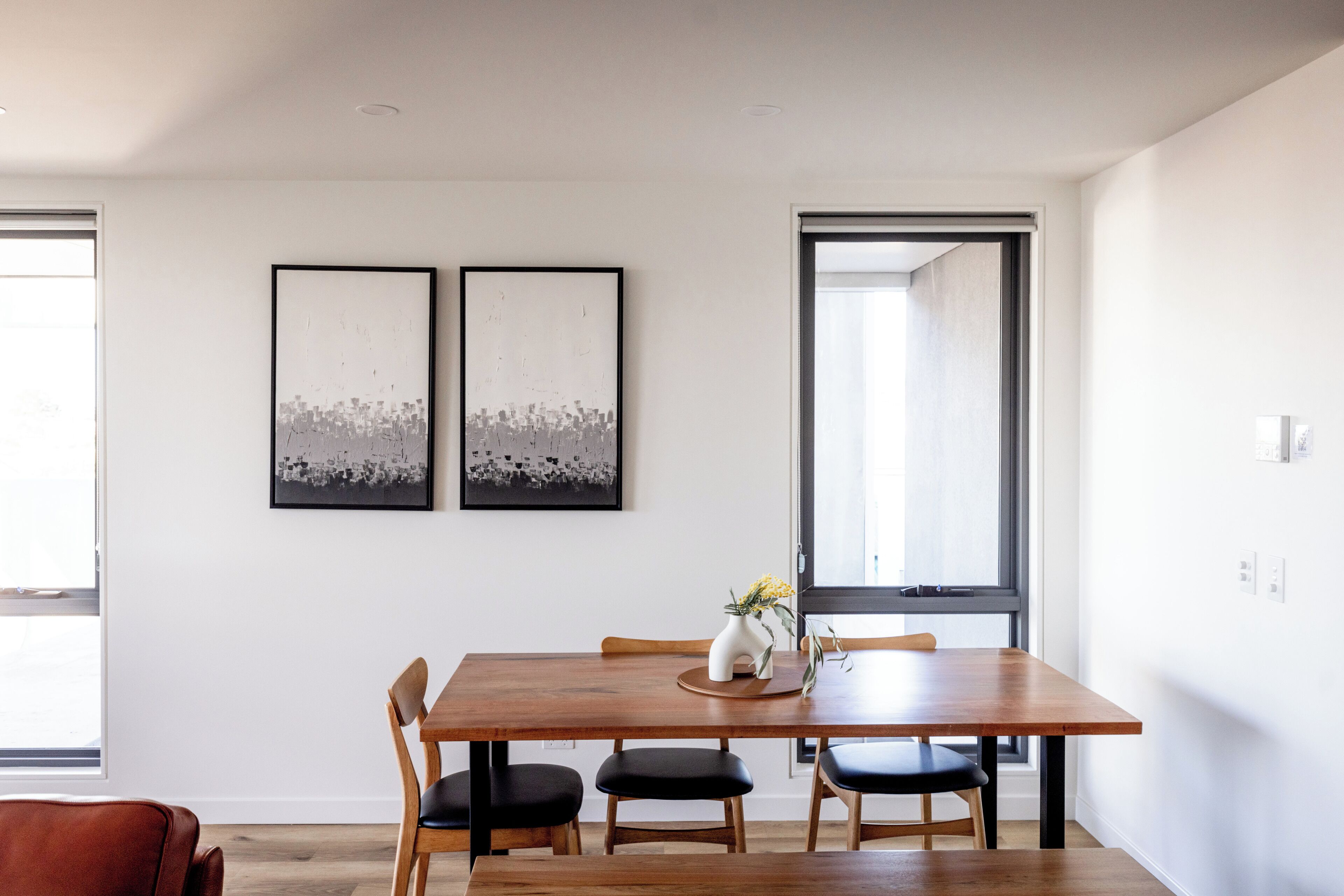 Un comedor con una mesa de madera, cuatro sillas y dos obras de arte enmarcadas en la pared.