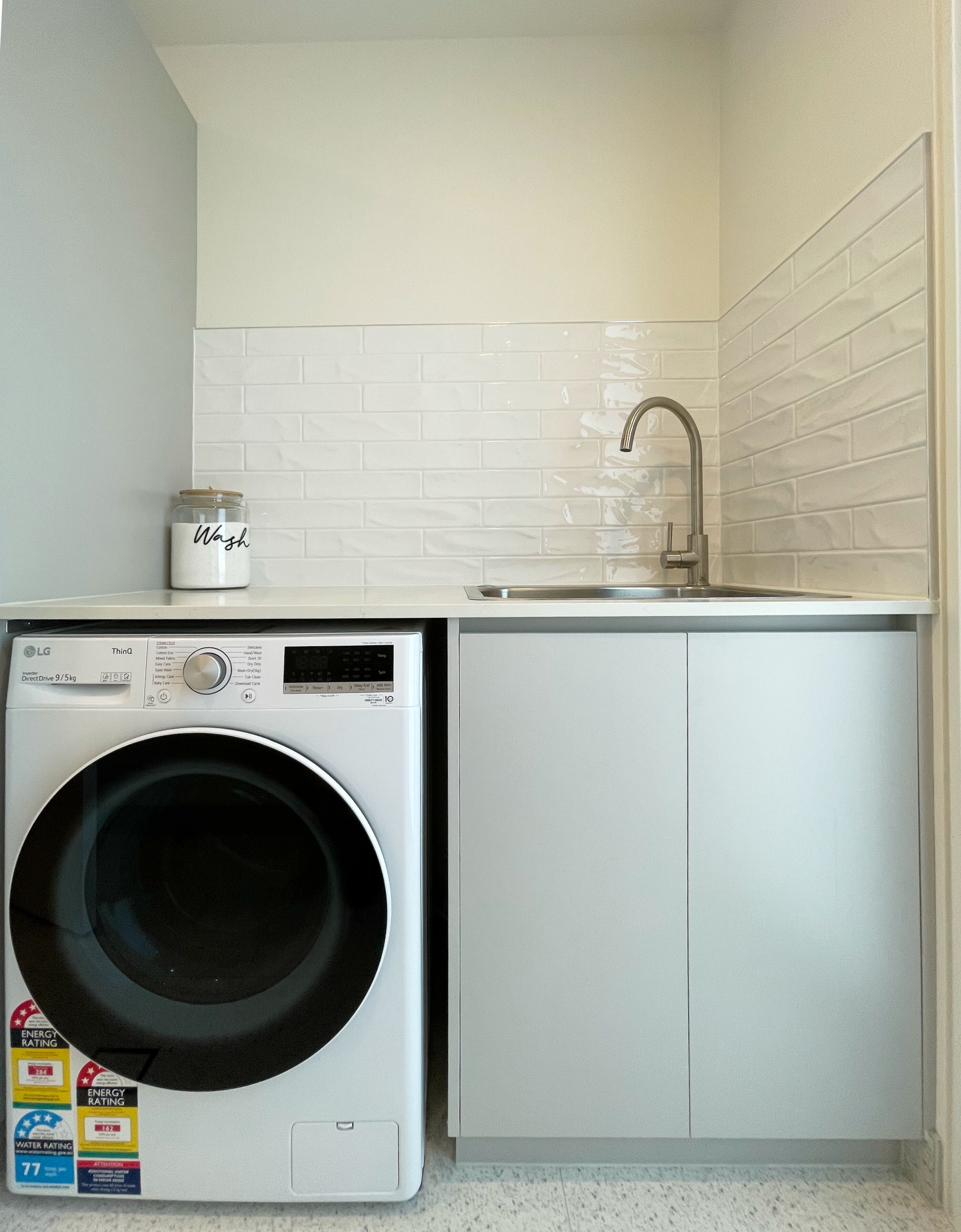 Een kleine wasruimte met een voorlader wasmachine, een wasbak en een kastje.