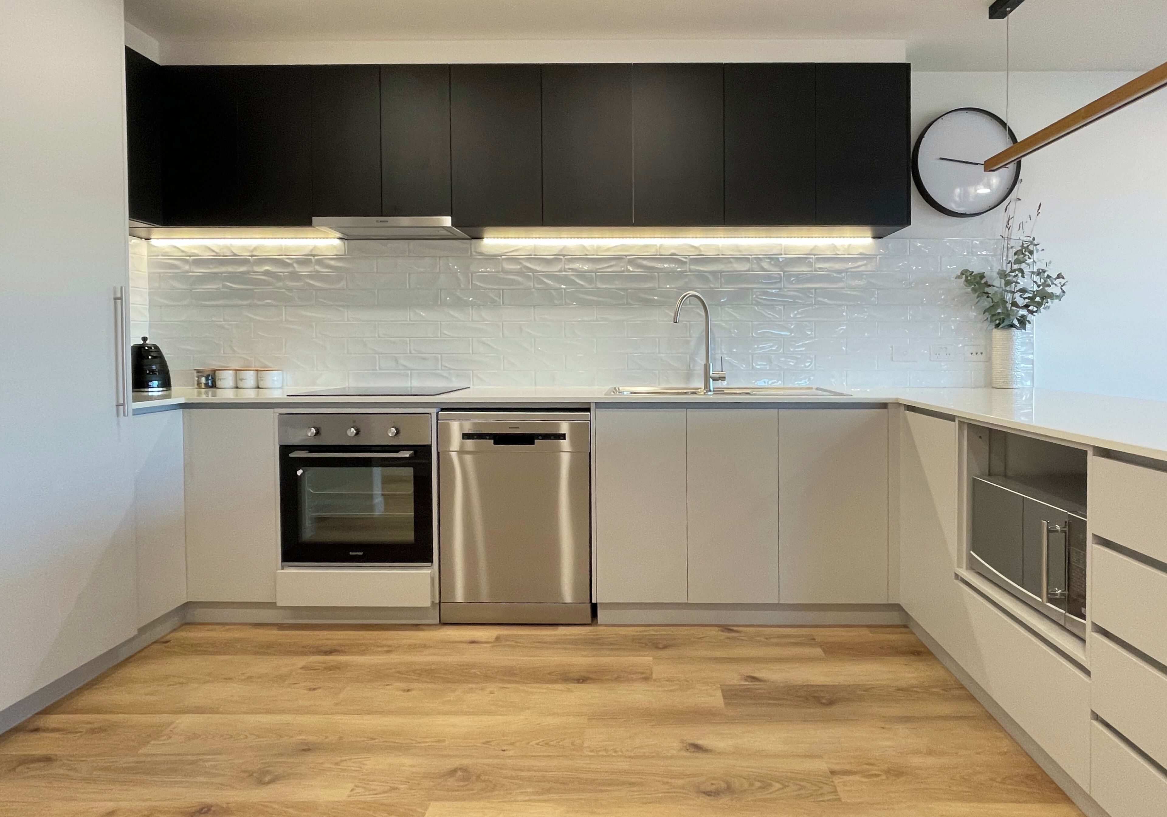 A modern kitchen with white cabinets, stainless steel appliances, and a wooden floor.