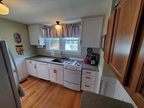 A kitchen with white cabinets, a stove, a sink, and a window with curtains.