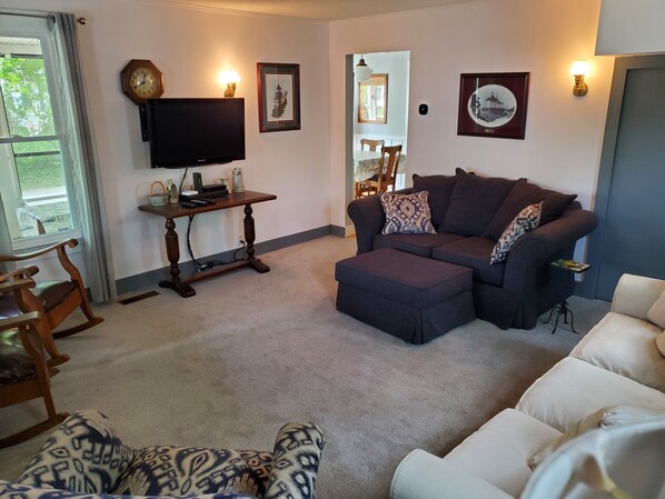 A living room with a sectional sofa, ottoman, and a television on a wooden stand.