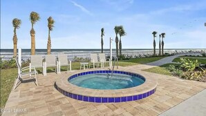 Uma área de piscina com hidromassagem, espreguiçadeiras e palmeiras.