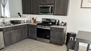 A modern kitchen with dark cabinets, a stainless steel stove, a microwave, and a granite countertop. - DREAM LAND (Porter)