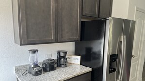 A kitchen with dark cabinets, a stainless steel refrigerator, a coffee maker, and a blender on a granite countertop. - DREAM LAND (Porter)