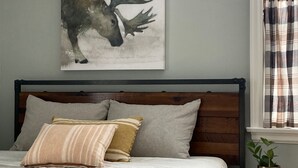 Ein Schlafzimmer mit einem Bett, Kissen, einem Kopfteil, einem Fenster mit Vorhängen und einem Wandbild von einem Reh.
