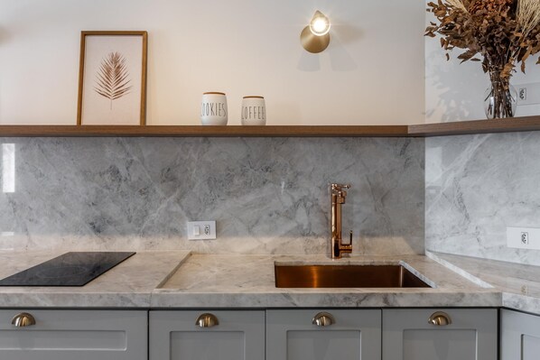 A kitchen with a marble countertop, a stainless steel sink, and a wall-mounted light fixture.