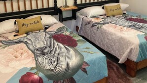 A bedroom with two beds, each with a floral bedspread and a 'stay awhile' pillow. There are two wall-mounted wreaths and a framed picture above the beds. - Gunner's Goat House at Billy Goat Mountain Village (Williamson)