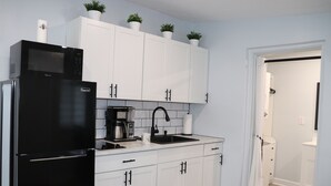Una cocina moderna con armarios blancos, un refrigerador negro, una cafetera y un lavamanos.