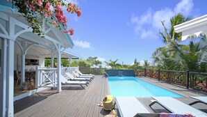 A wooden deck with a pool, lounge chairs, and a covered seating area.