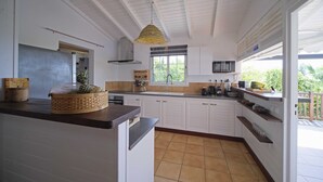 A kitchen with white cabinets, a wooden countertop, a hanging light fixture, and a window with a view of greenery.