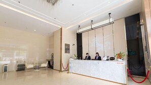 Een hotel receptie met een marmeren balie, twee receptionisten en een rode lintbarrière.