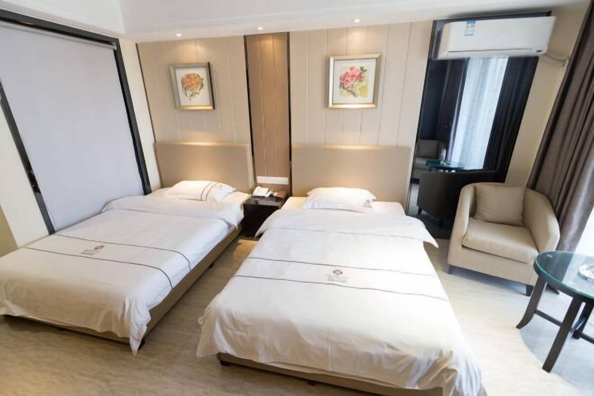 Een hotelkamer met twee eenpersoonsbedden, een slaapbank, een tafeltje en een raam met gordijnen.