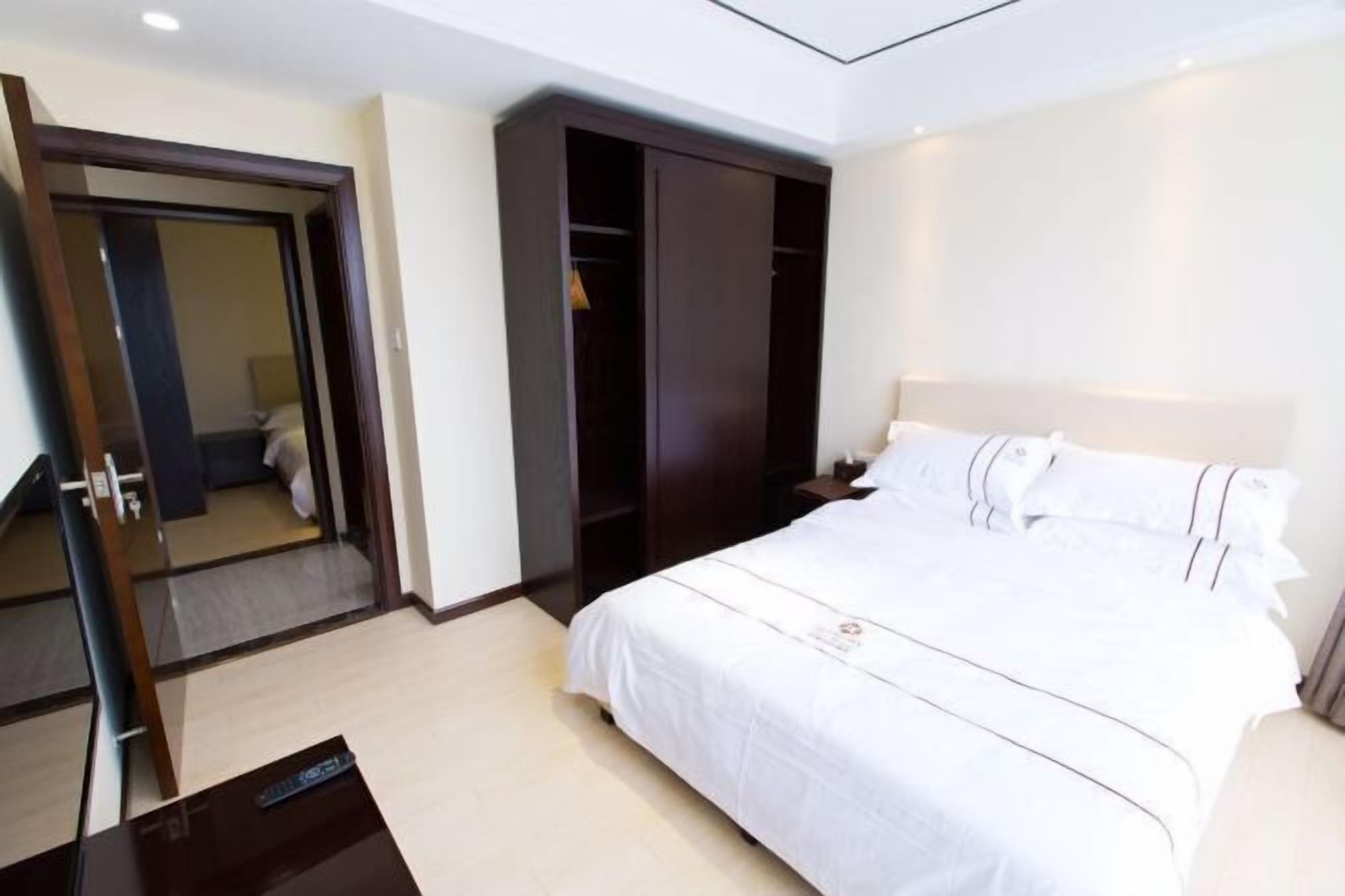 Una habitación de hotel con una cama grande, un armario y un escritorio con un control remoto.