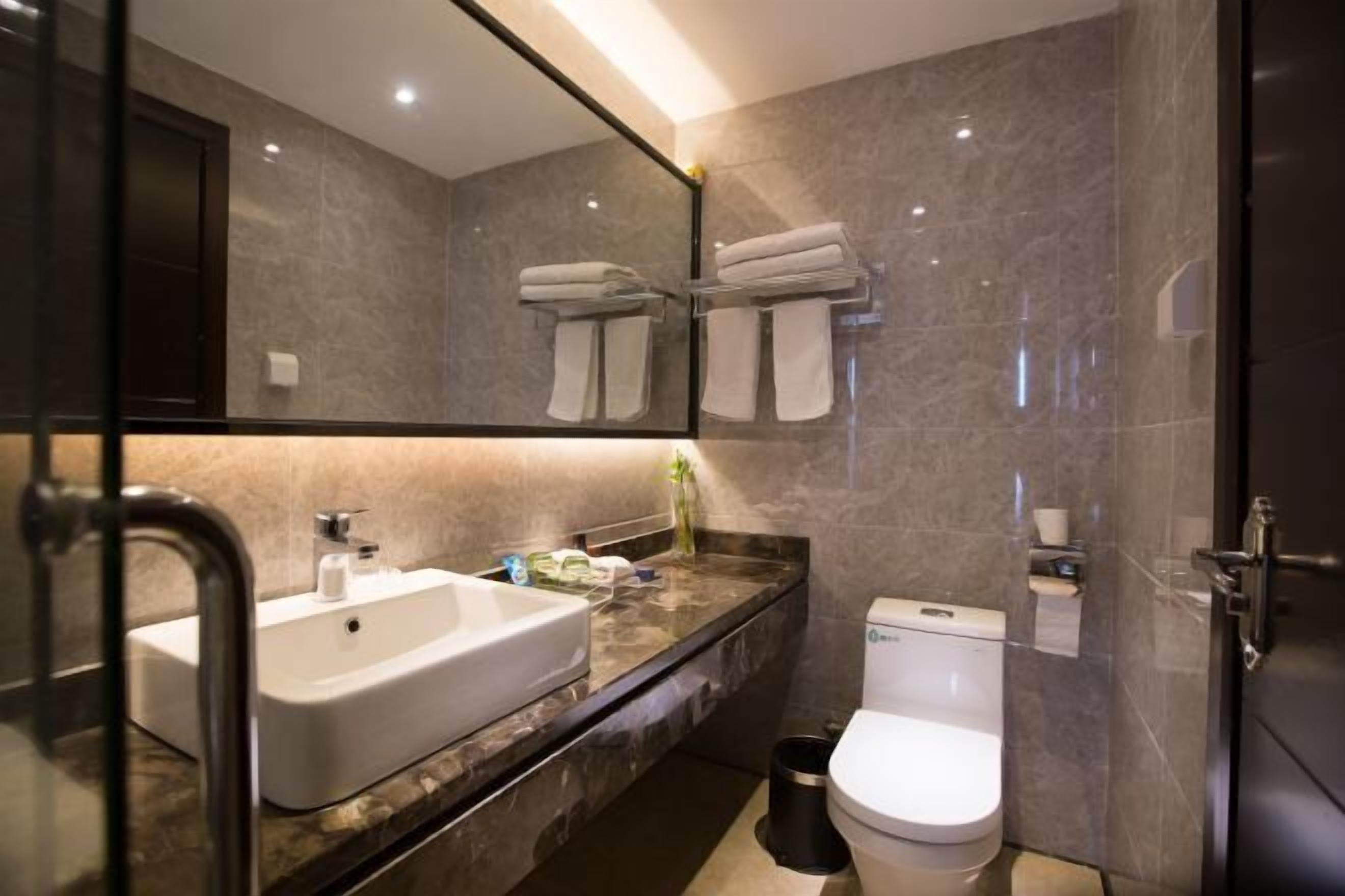 A modern bathroom with a large mirror, a sink, a toilet, and a glass shower enclosure.