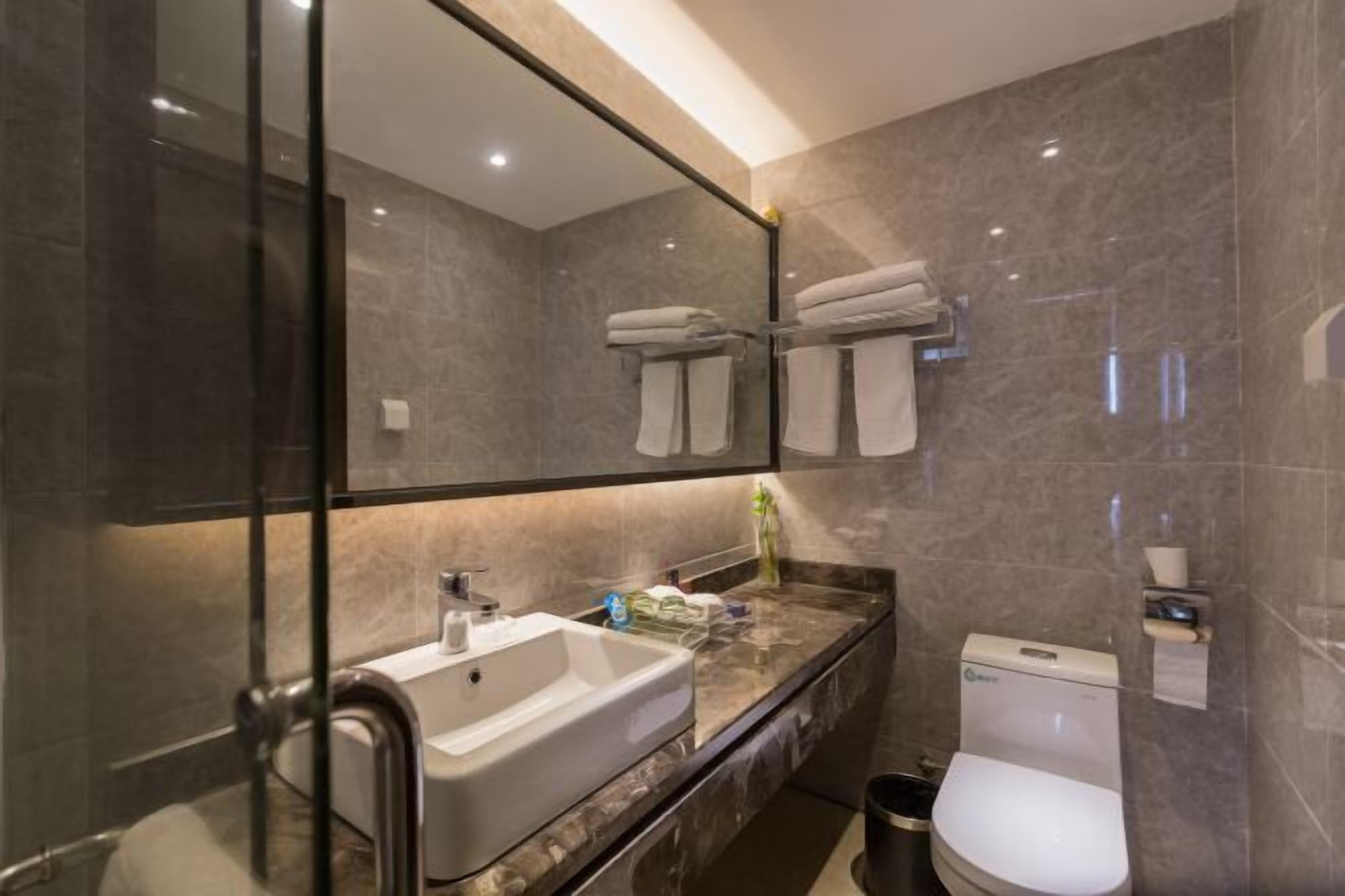 A modern bathroom with a large mirror, a sink, a toilet, and a towel rack.