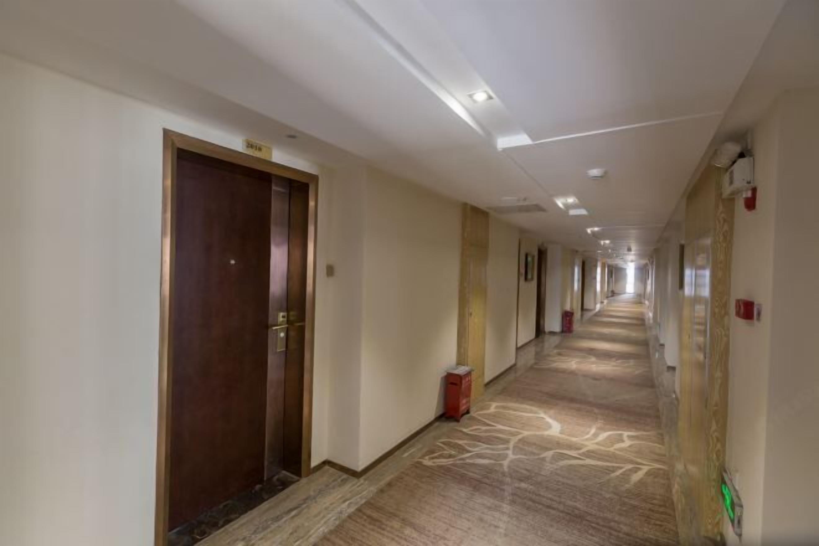 A hotel corridor with a carpeted floor, wooden doors, and a ceiling with recessed lighting.