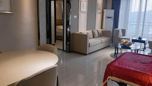 Een moderne hotelkamer met een bank, een eettafel, een bed met een rode spreiding en een bijzettafeltje met decoratieve objecten.
