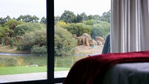 Una habitación con un amplio ventanal que da a un jardín ajardinado con un estanque y árboles.